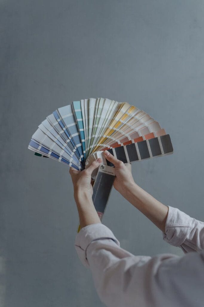 pexels-photo-6474446 Hands displaying a fan of paint color swatches against a gray wall, ideal for home renovation projects.