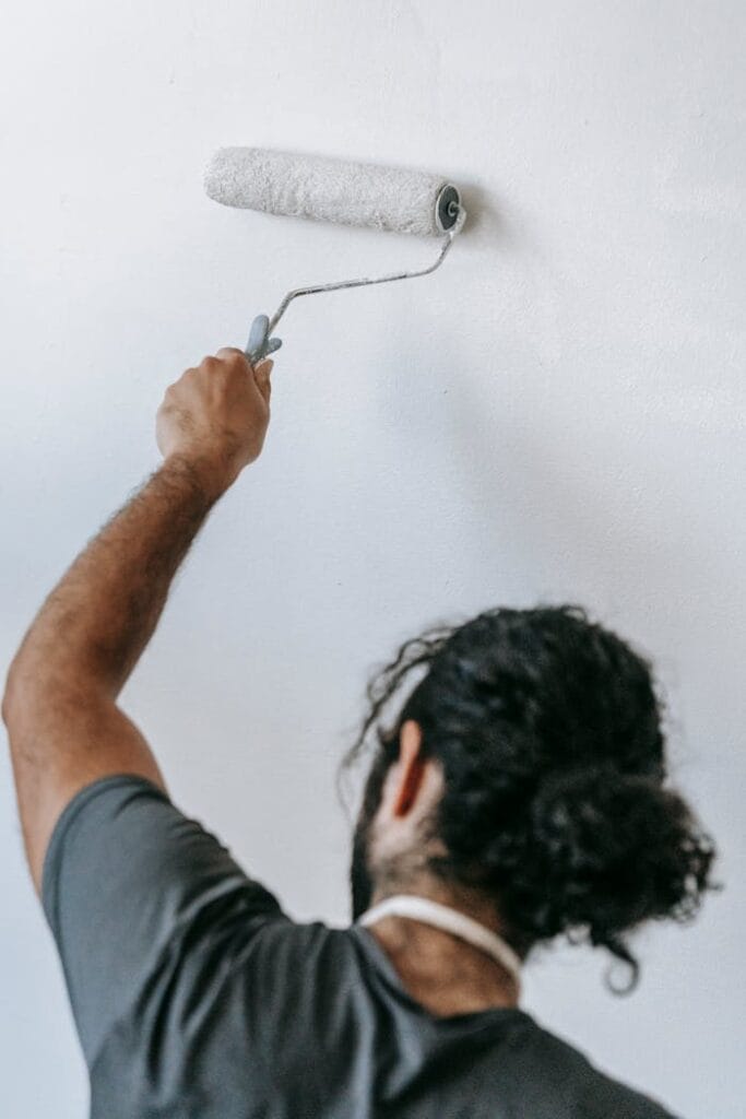 pexels-photo-7218001 A man painting a wall white with a roller, focusing on home renovation.